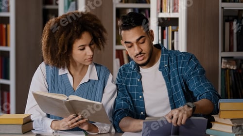 Preview: Two diverse students sitting in university library preparing for exam studying young guy arguing