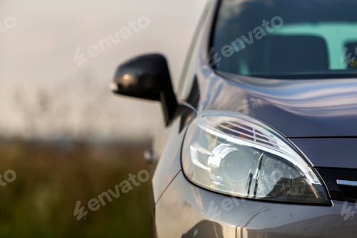 Preview: Close-up detail part of black shiny car-headlight, mirror, hood and radiator grille on blurred