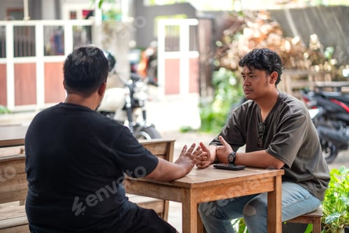 Preview: Two Asian Men Chatting Over Coffee at Outdoor Cafe in Indonesia