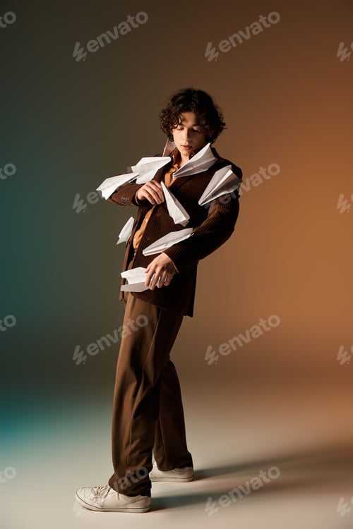 Preview: Curly haired young man displays unique style with paper planes in trendy studio setting