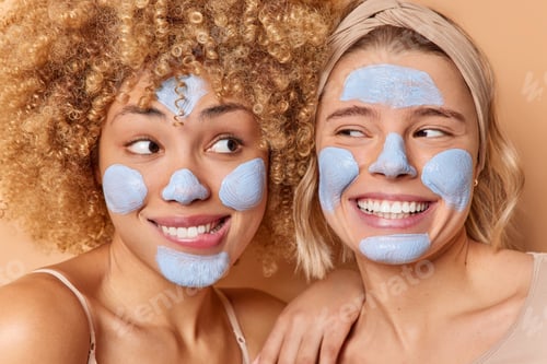 Preview: Close up shot of positive two young European women apply beauty mask for skin treatment smiles gladf