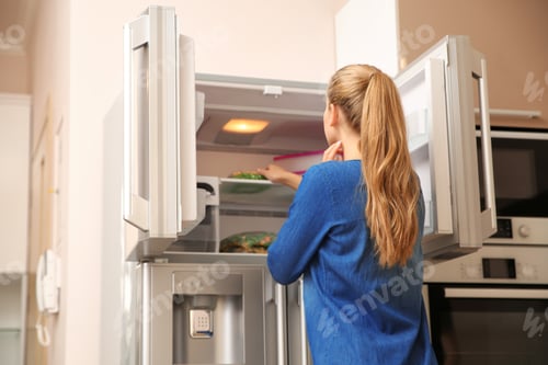 Preview: Young woman choosing food in refrigerator at home