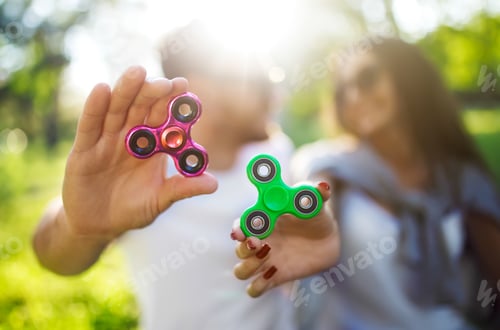 Preview: Young girl and boy playing with fidget spinners in the park. stress relieving toy. Sunny summer day.