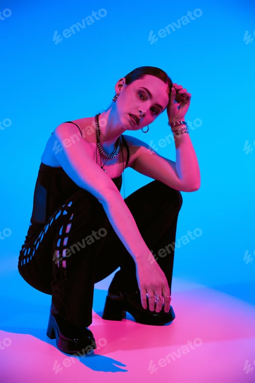 Preview: Stylish young woman poses in trendy outfit with vibrant pink and blue backdrop