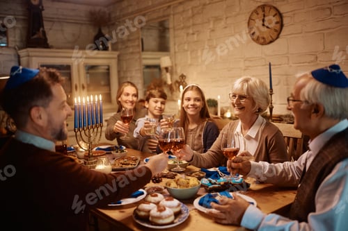Preview: Happy extended family celebrating Hanukkah and toasting while having dinner at dining table.