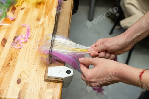 Preview: Crafting yarn: female hand combing colorful wool fiber on wooden table
