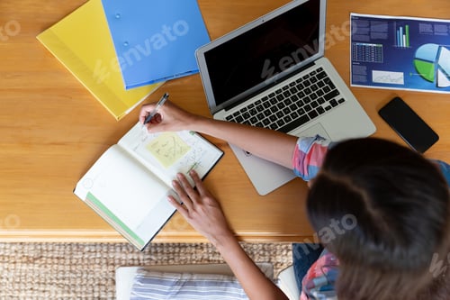 Preview: Caucasian woman sitting by desk working from home using laptop