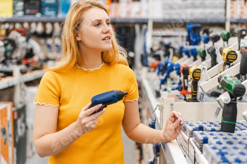 Preview: Happy young woman choosing electric screwdriver, diy, standing in construction store