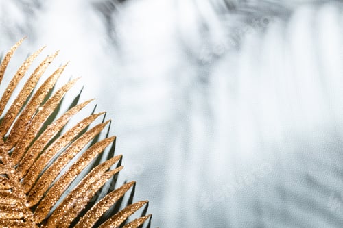 Visualização: Folhas de palmeira douradas e sombras em um fundo de parede azul.