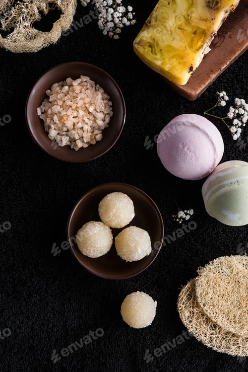 Preview: top view of handmade soaps, sea salt and small white flowers on black sponges