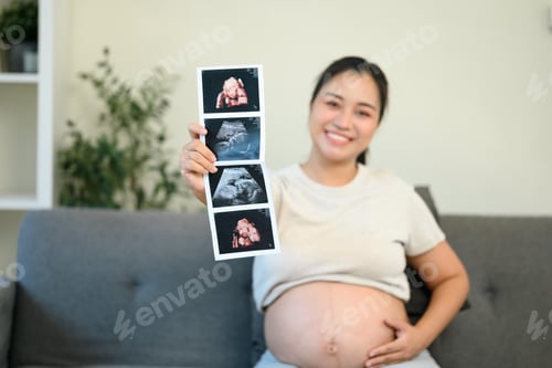 Preview: Happy expectant mother proudly showing ultrasound photos while gently touching her bare belly