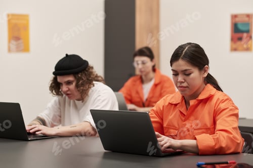 Preview: Young Adult Women in Prison Uniforms Studying on Laptops in Classroom Setting