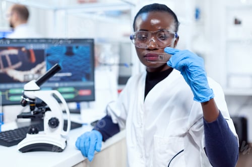 Preview: Concentrated view of african scientist holding glass microscope glass