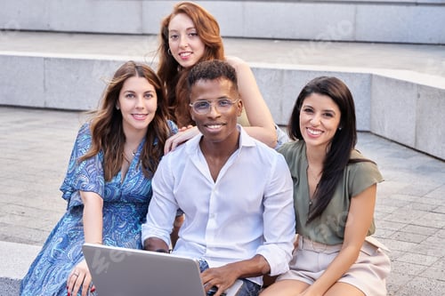 Preview: Group of multiracial people looking at camera and smiling while using a laptop outdoors