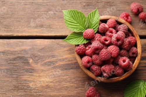 Preview: Fresh ripe raspberries in bowl and green leaves on wooden table, flat lay. Space for text