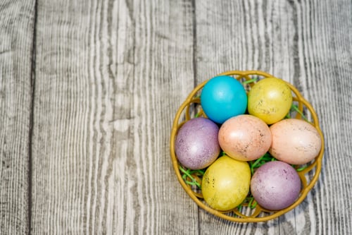 Preview: A basket with multi colored easter eggs on the wooden background. Space for text. Easter Holiday.