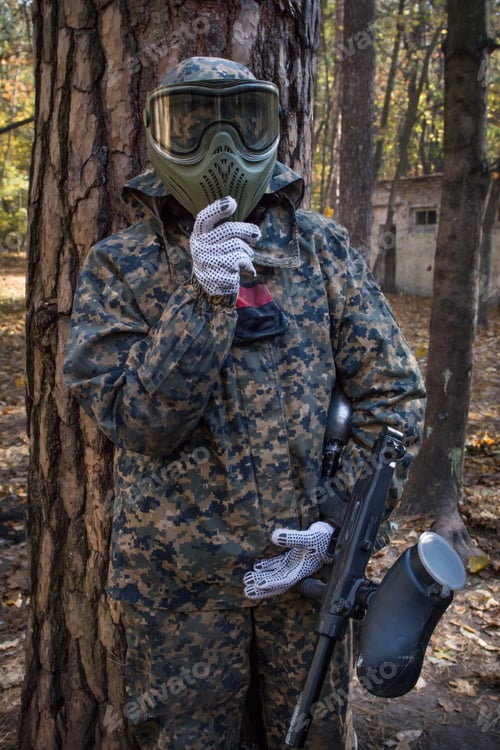 Preview: Paintball player in protective uniform over shelter
