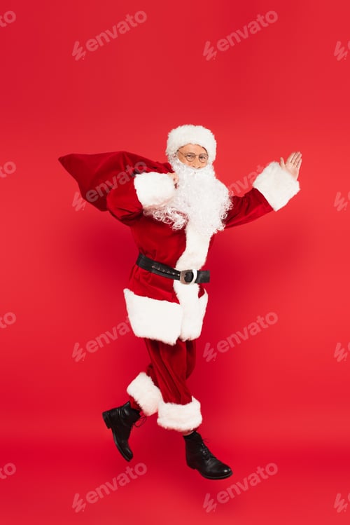 Preview: Santa claus with sack pointing with hand and levitating isolated on red