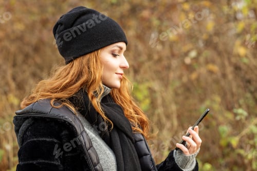 Preview: young woman with mobile phone in autumn park. Black hat and scarf.