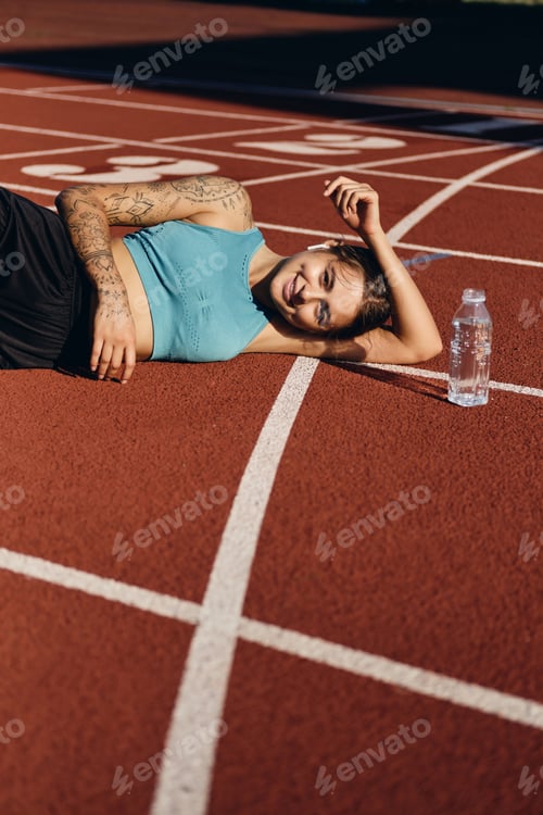 Preview: Glad smiling athlete girl lying on runner track after workout happily looking in camera on stadium