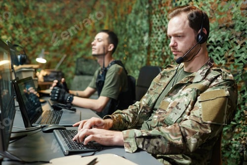 Preview: Serious young male operator in camouflage uniform typing on keyboard