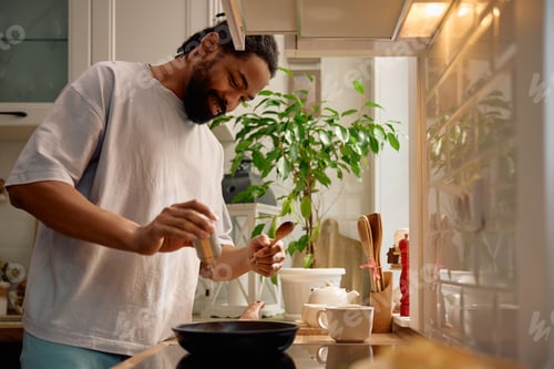 Preview: Happy black man preparing himself a breakfast in the kitchen.