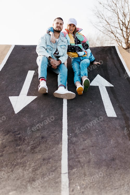 Preview: Young couple sitting between the signs on the floor of a skate park