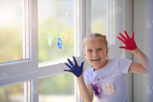 Preview: Portrait of a happy little girl draw palms on the window.