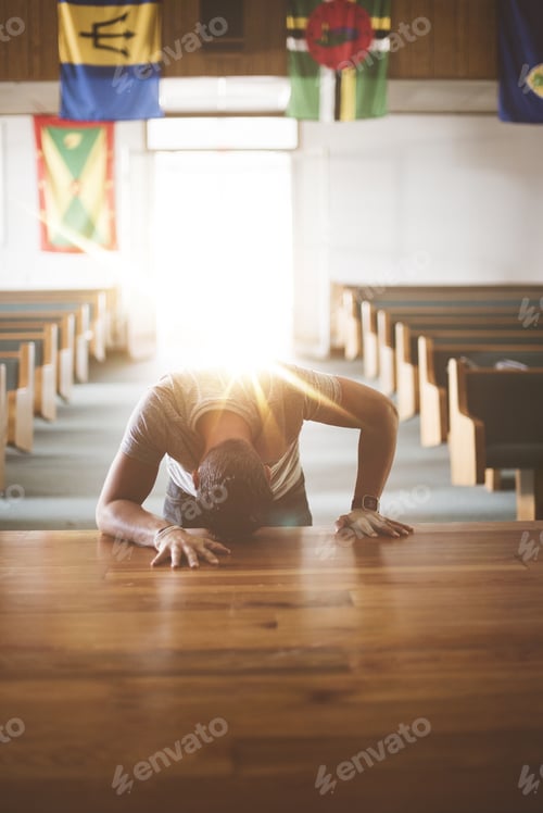 Preview: Vertical shot of a male with his head on a wooden surface in the church praying