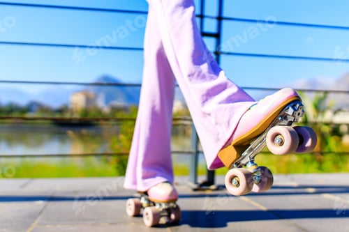 Preview: close up photo of feet of woman in flared pink pants skating on rollers in park