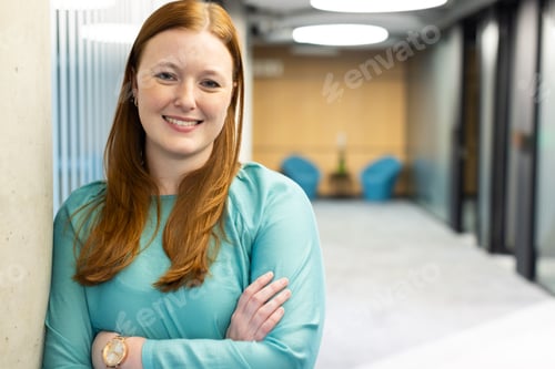 Preview: Smiling businesswoman in office, crossing arms and leaning against wall, copy space