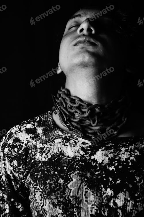 Preview: Vertical portrait of a young asian man with a metal chain around his neck in grayscale