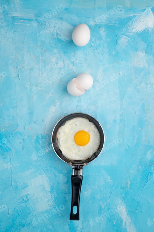 Preview: top view of frying pan with fried egg and eggshell with egg on blue background with copy space