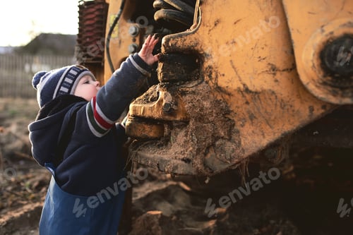 Preview: A boy in the village on the background of a tractor walks on the sand .