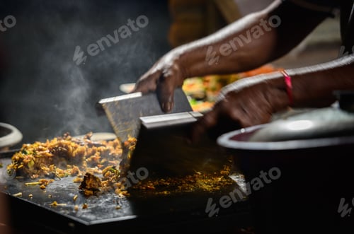 Preview: Hands of the kottu roti vendor, making kottu on top of a steel grill plate