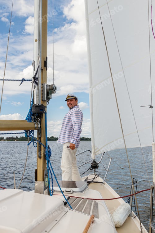 Preview: sailor man in a cap on a boat under sail against the sky and water