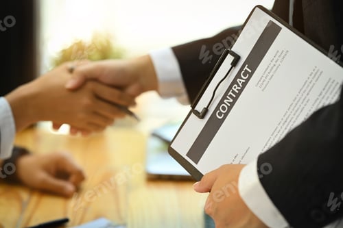 Preview: Real estate broker holding contract clipboard while shaking hands with client.
