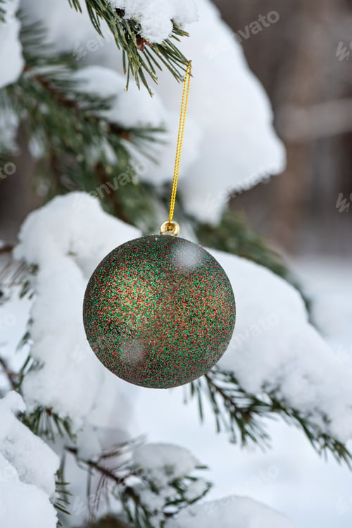 Preview: Hanging green glitter Christmas ball on spruce and over blurred background