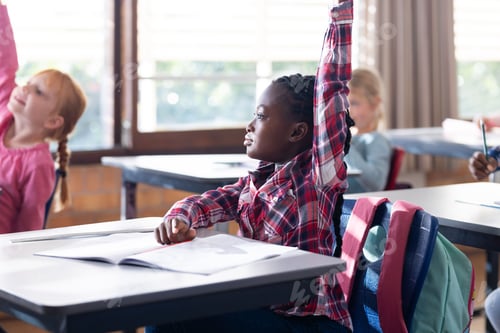Preview: In school, african american girl raising hand while sitting at desk with open notebook