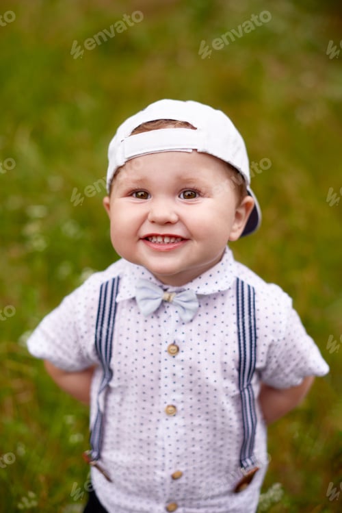 Preview: happy little boy play in grass in summer, smiling with teeth and look in camera. world children day