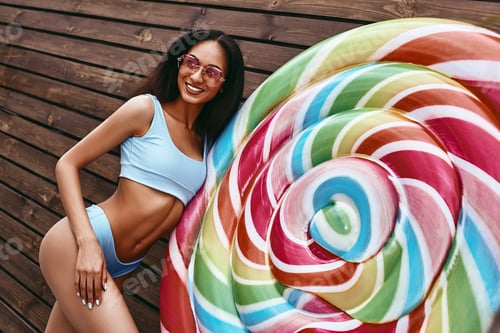 Preview: Salt in the air. Sand in my hair. African american model posing in bikini near big colorful lollipop