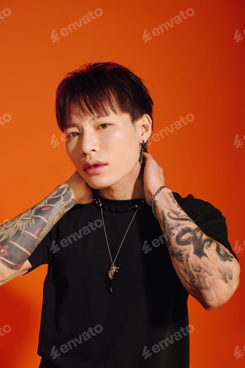 Preview: Stylish young asian man poses confidently against a vibrant orange background in a trendy outfit