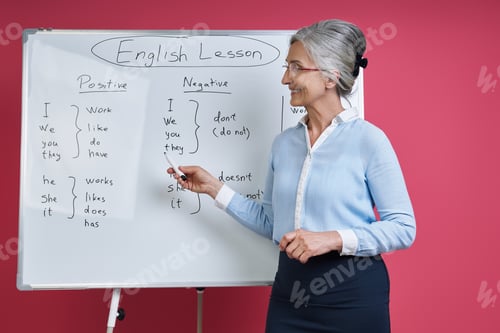 Preview: Senior woman teaching English language while standing near the whiteboard against pink background