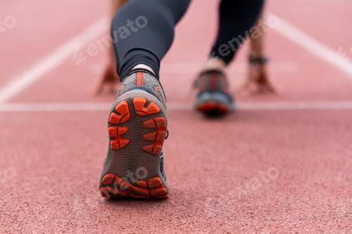 Preview: close-up of runner legs in low start position, prepared to race along urban outdoor stadium track