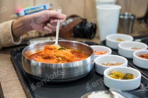 Preview: Hand using spoon scooping spicy kimchi soup and vegetable pickle on cup