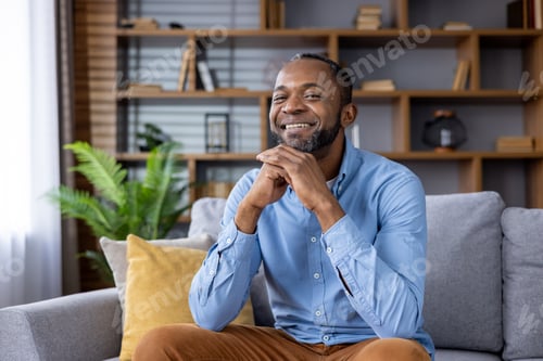 Preview: Smiling man relaxing at home on a couch with comfortable and cozy living room interior