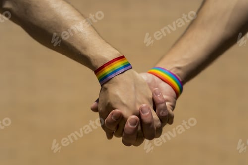 Aperçu: Two Caucasian men holding hands with a rainbow-patterned wristband against a brown background