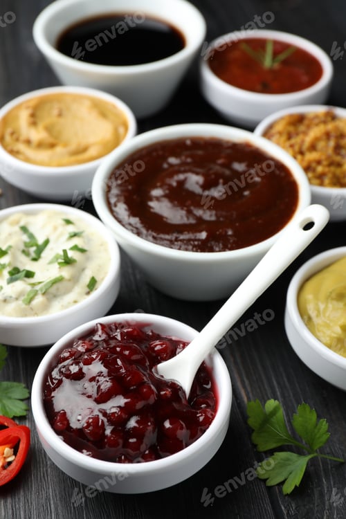 Preview: Different tasty sauces in bowls, parsley and chili pepper on black wooden table