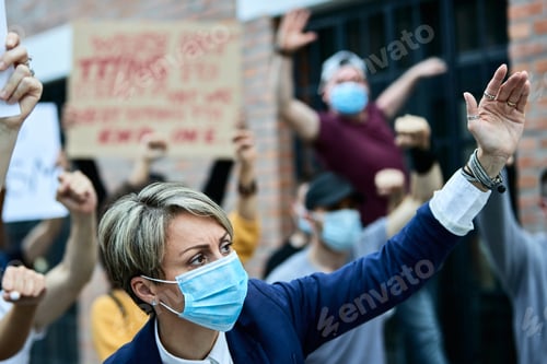 Preview: Businesswoman with face mask with raised arm on a protest during COVID-19 epidemic.
