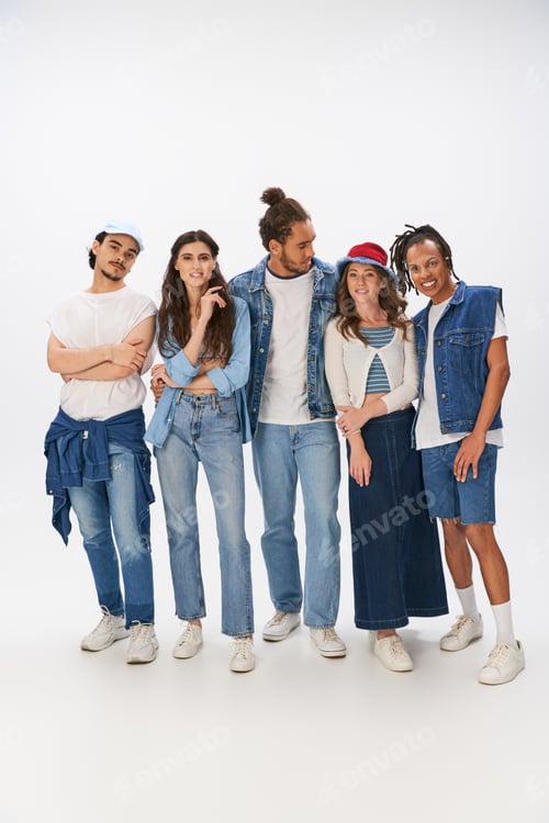Preview: full length of interracial friends in trendy outfits and denim wear standing in grey backdrop